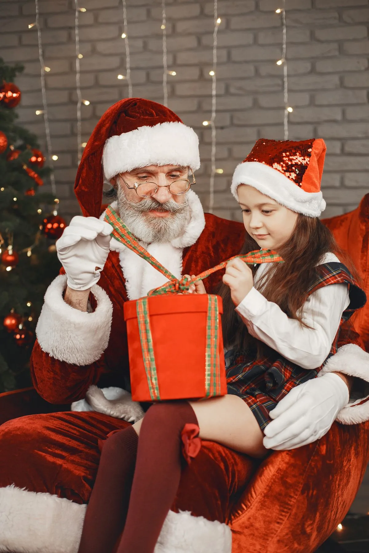 Santa Claus helping a young girl open a wrapped Christmas present